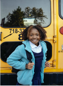 An African-American Girl Wearing a Zipper Hoodie and Bag, Posing Outside a Yellow School Bus