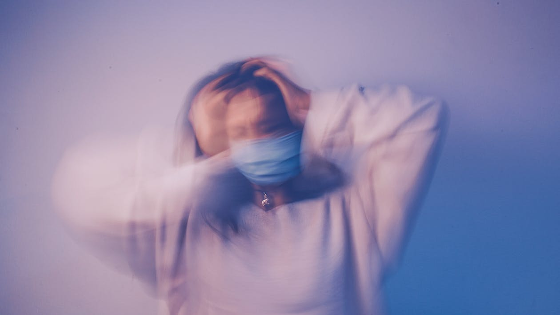 Faded Image of a Masked Female Holding Her Head in Distress