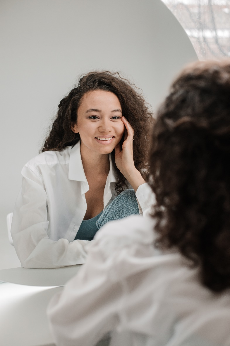 Curly-haired woman smiling at her reflection in the mirror.