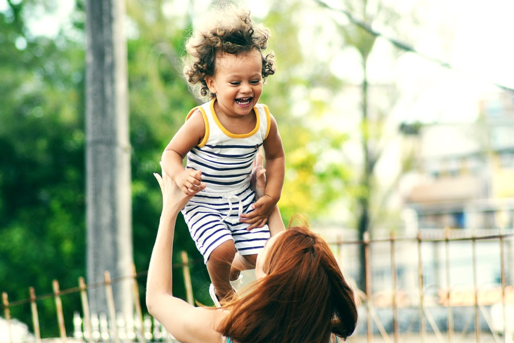 A happy toddler being lifted in the air by their parent