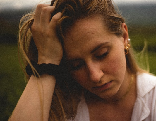 A woman struggling with physical health problems keeps her hand against her head as she looks down.