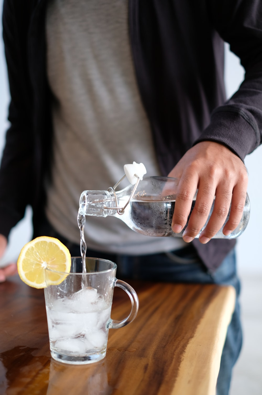 A Faceless Person in the Process of Pouring Water into an Ice-Filled Cup Garnished with a Slice of Lemon